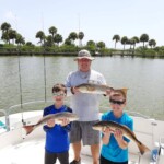Fishing adventure with kids and guide at Cast Away Adventures , featuring caught fish on a boat in a scenic waterway with lush palm trees in the background.