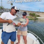 Cast Away Adventures fishing trip with a man and woman holding a permit on a boat, featuring sunny skies and Florida coastal scenery.